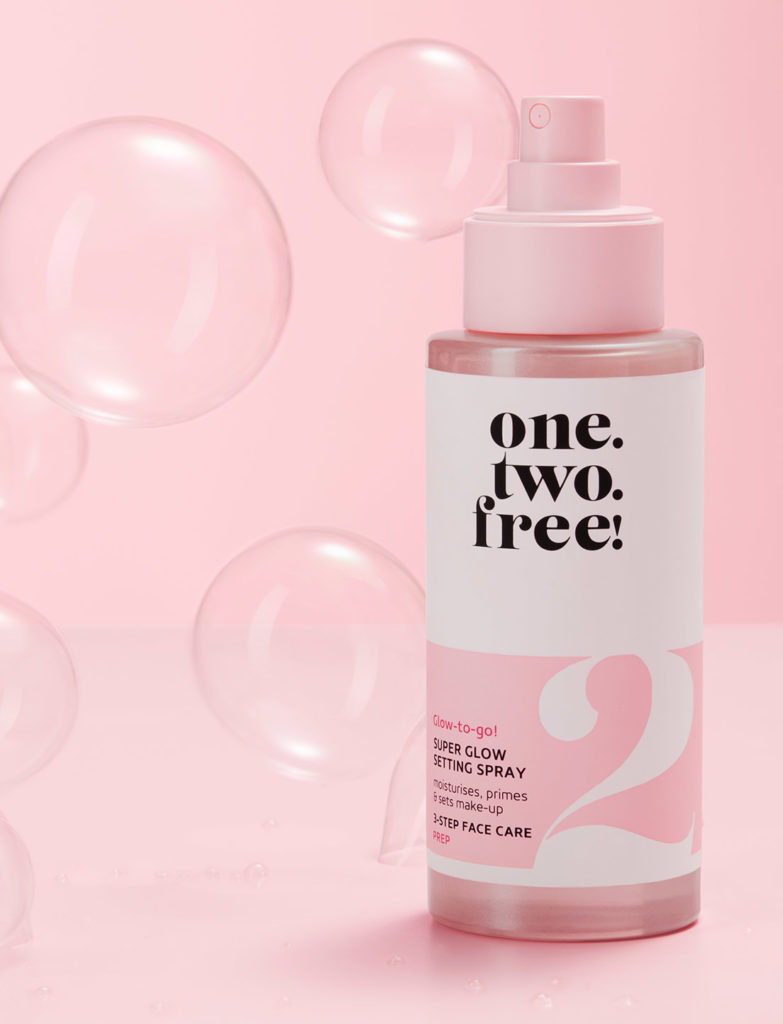 Product Super Glow Setting Spray in front of a pink wall with soap bubles on the background