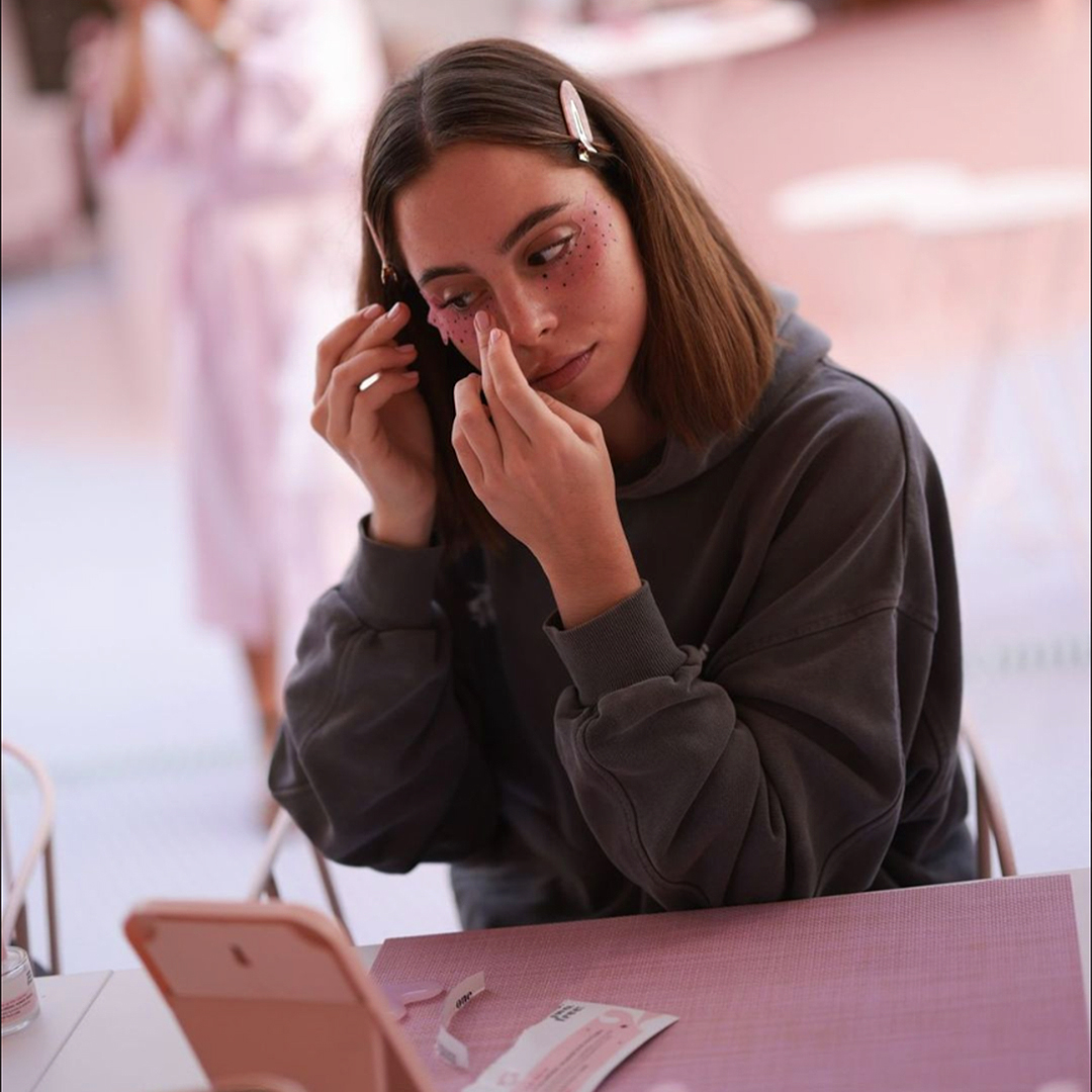 A woman sits in front of a mirror and applies anti-ageing eye pads